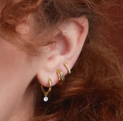 Gold huggie hoop earrings styled on pierced ear alongside ear cuff and charm hoop