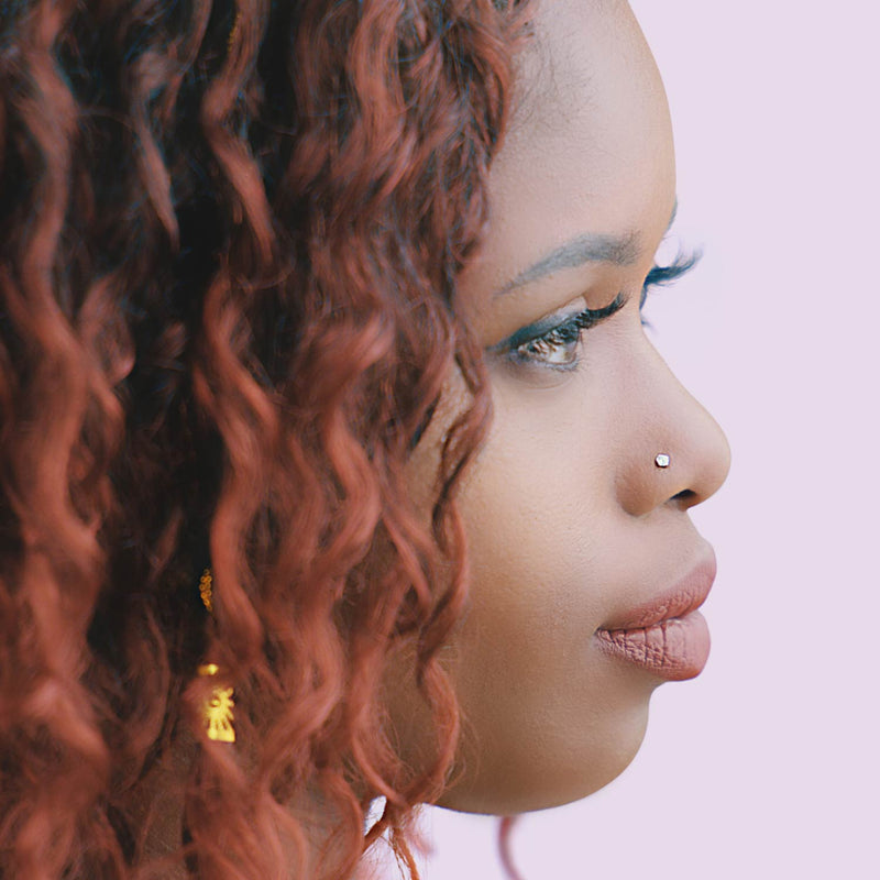 Diamond flat back stud worn in nose piercing on model with curly auburn hair, profile view