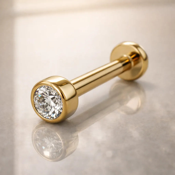 14k yellow gold 3mm CZ bezel flat back labret resting on marble surface, lifestyle angled shot