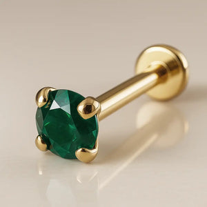 14K yellow gold flat back labret with 2mm prong-set emerald, angled product shot on beige surface