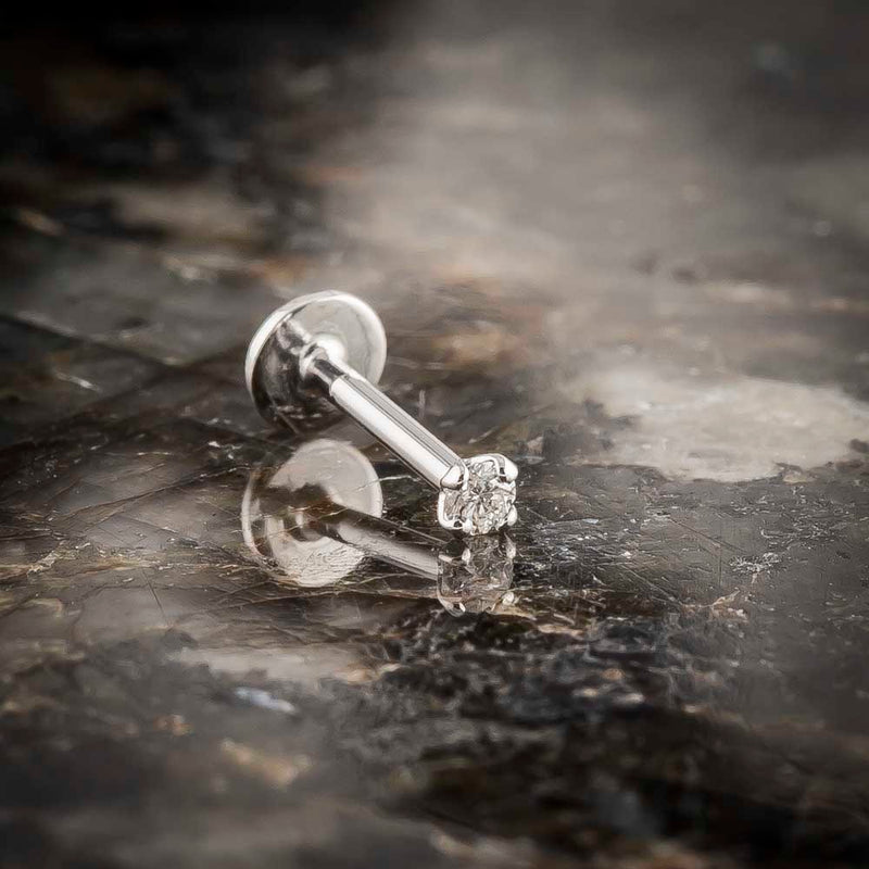 14k white gold 2mm diamond flat back labret stud resting on dark stone surface, lifestyle shot