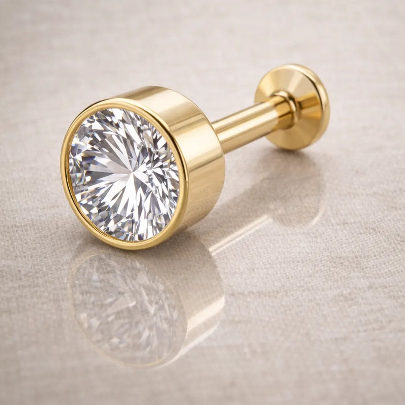 14k yellow gold 4mm CZ bezel-set flat back labret resting on linen surface, side angle view