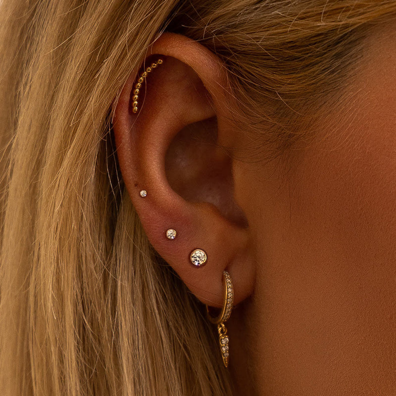14k gold diamond bezel flat back stud styled in a curated ear with multiple gold cartilage piercings