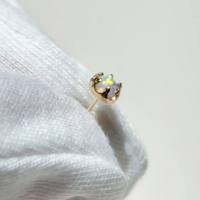 A gold crown-shaped stud earring with an iridescent opal-like center stone, held by white gloves.