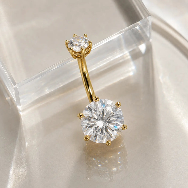 Astra II belly ring in yellow gold with moissanite gemstone on a glass surface.