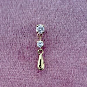 14K yellow gold dew drop labret stud with dual CZ stones, shown on textured surface for scale