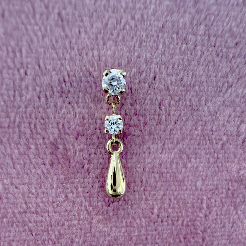 14K yellow gold dew drop labret stud with dual CZ stones, shown on textured surface for scale