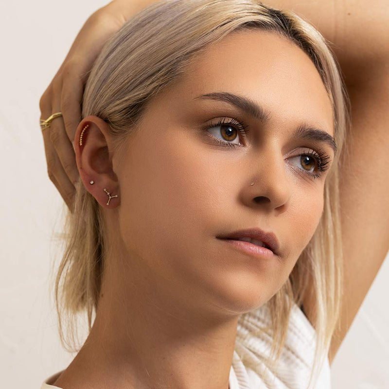 Virgo constellation 14k gold flat back earring worn in model's lobe piercing, styled ear stack