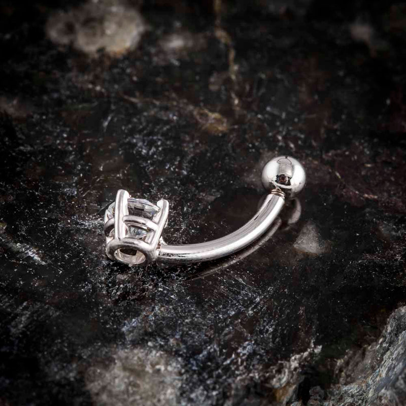 Side profile of 14k white gold diamond navel ring showing curved barbell and prong setting on dark stone surface