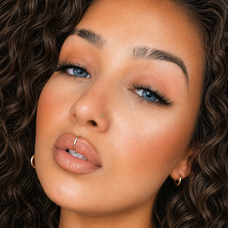 Model wearing four-diamond gold seam ring as a lip piercing hoop with nose stud styling