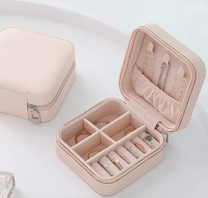 Pink travel jewelry box open showing ring rolls and earring pockets storing gold and crystal rings