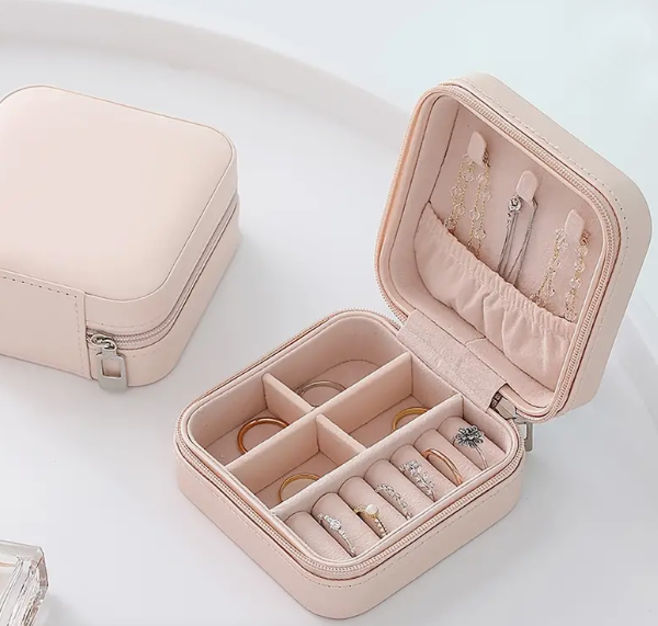 Pink travel jewelry box open showing ring rolls and earring pockets storing gold and crystal rings