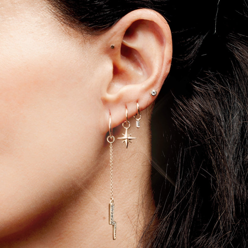 Gold north star charm on a hoop earring in a layered ear stack, side profile showing dangle fit