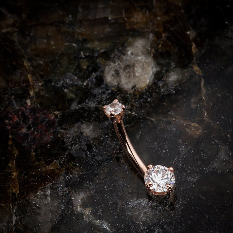 14k rose gold diamond navel ring resting on dark marble surface, angled lifestyle shot