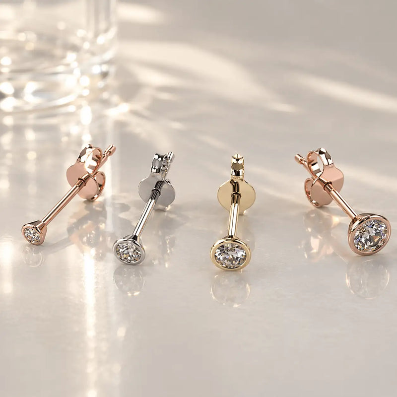 14K rose gold, white gold, and yellow gold bezel diamond stud earrings laid flat showing post and butterfly backs