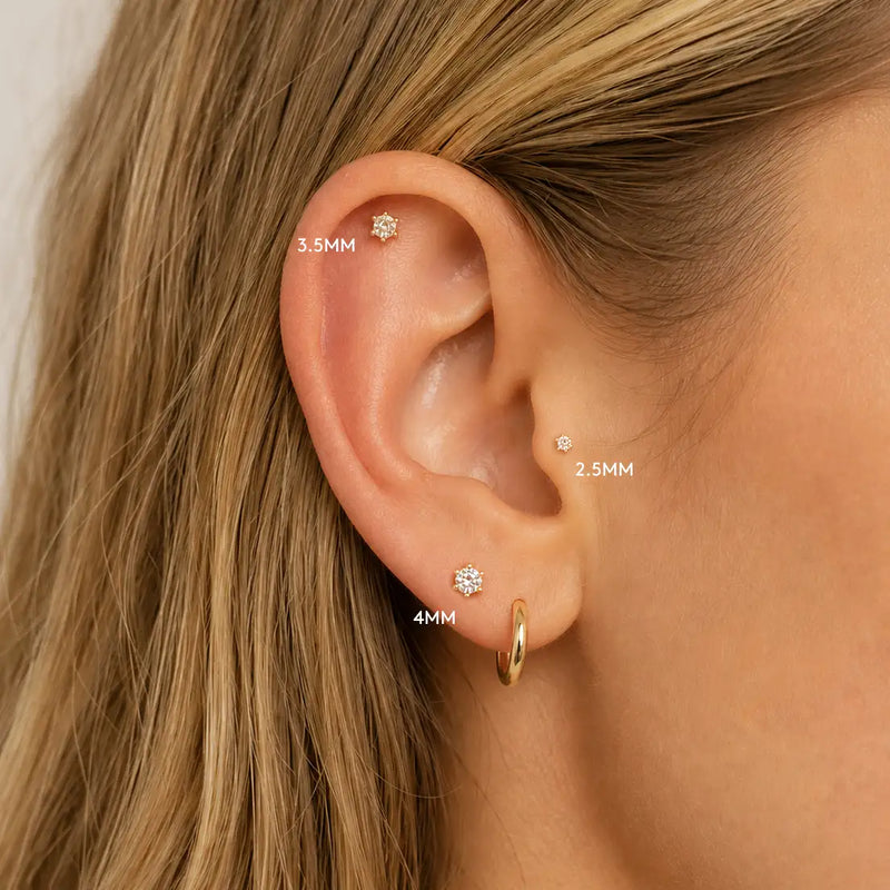 Close-up of an ear with gold Astra diamond earrings and measurements labeled.