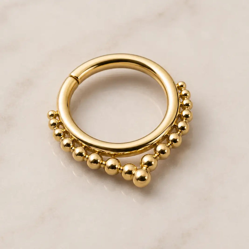 Gold seam ring septum piercing jewelry with bead detailing on a beige background