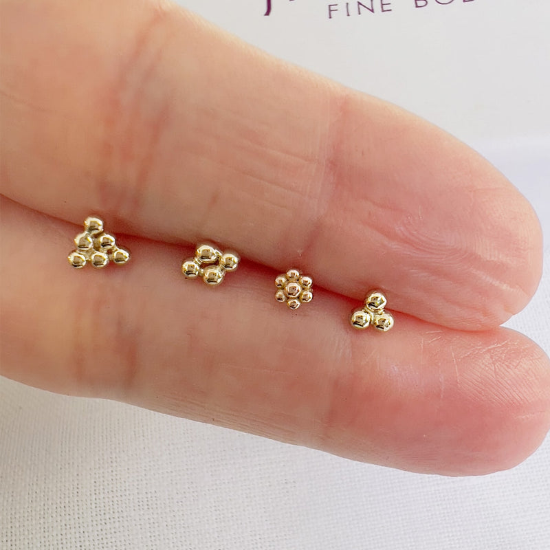 Four 14k gold trinity bead cluster ends in varying sizes held on fingertip for scale reference