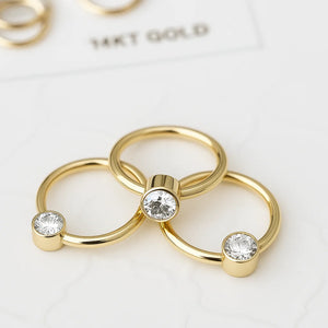 Three 14k yellow gold CZ bezel fixed bead rings in varied sizes next to a 14KT gold authenticity card