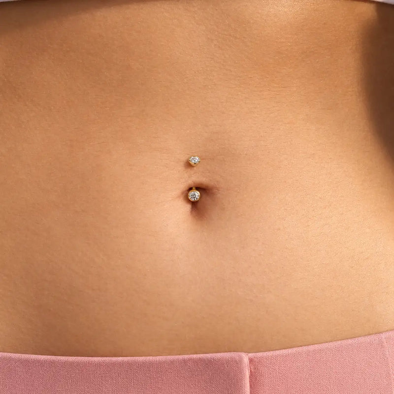 Close-up of a model's belly button piercing with a 4mm bezel-set curved barbell - two clear stones set in 14k yellow gold