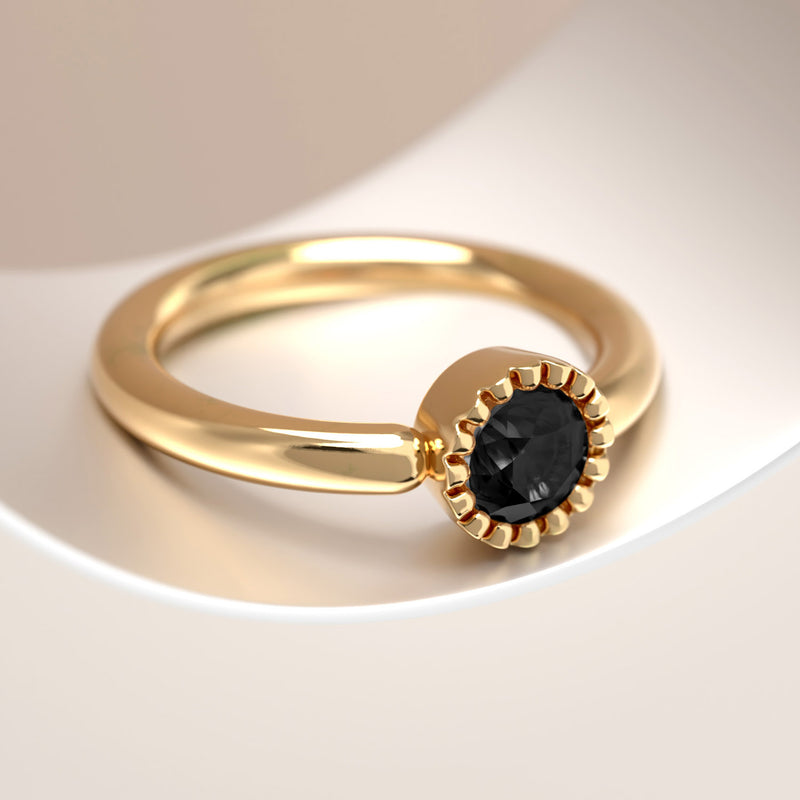 Close-up of black diamond milgrain bezel setting on 14k yellow gold captive bead ring, warm background