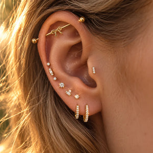 14k gold bow industrial barbell shown in ear piercing styled with multiple gold cartilage jewelry