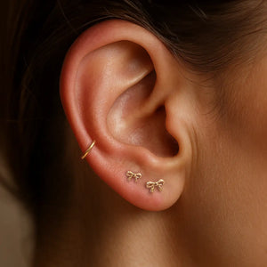 14k gold mini bow flat back studs worn in two lobe piercings, styled with a gold ear cuff