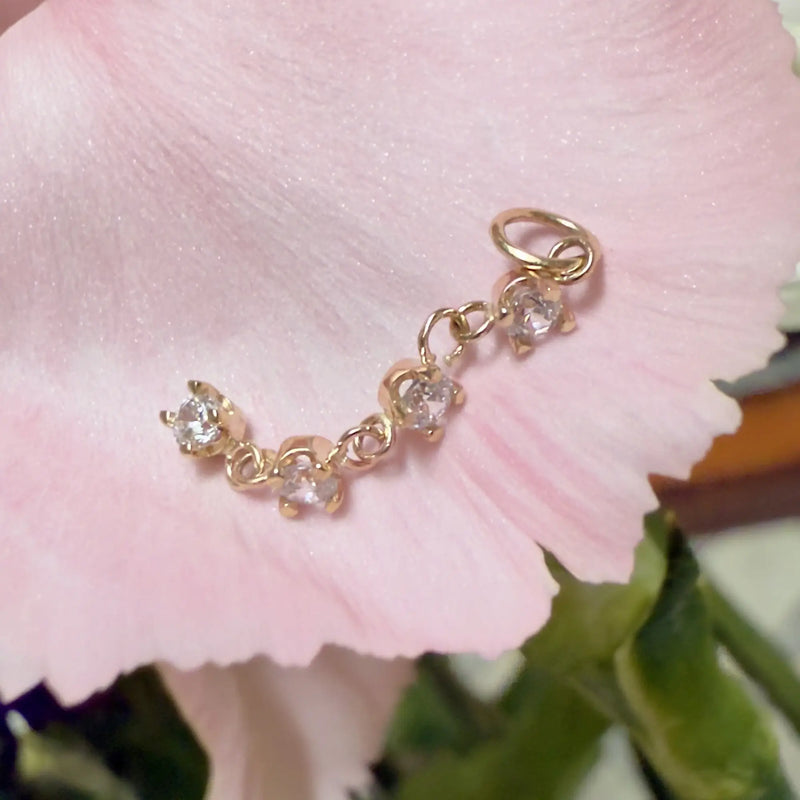 14k gold four-stone CZ piercing charm resting on a pink flower petal, angled lifestyle view