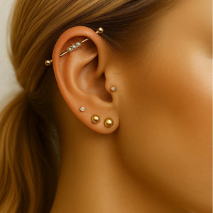 Gold bubble cabochon industrial barbell shown in ear piercing alongside stacked gold earrings