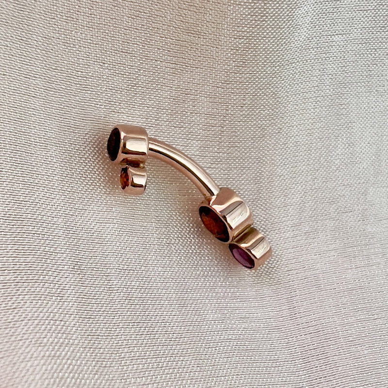 Side profile of 14k rose gold garnet bubble bezel belly ring showing curved barbell shape