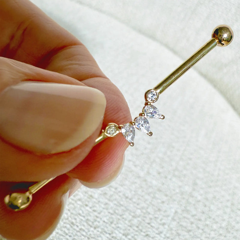 14k gold Celeste Arc industrial barbell held in hand, showing pear and round CZ stone detail