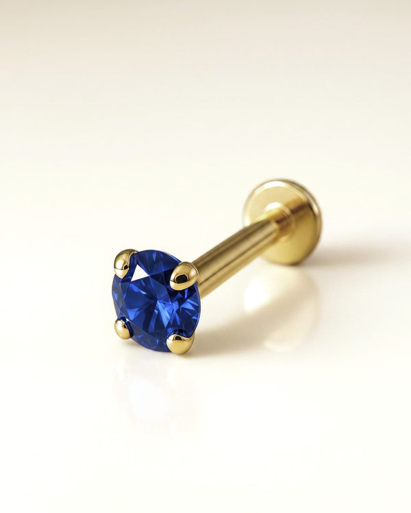 The Color Shop flat back studs - 2mm blue sapphire prong-set 14k yellow gold flat back stud on a cream ground