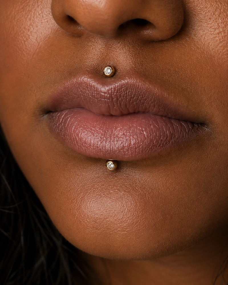 Cyber bites piercing with gold bezel-set studs in the Medusa and labret positions, one above the upper lip and one below the lower