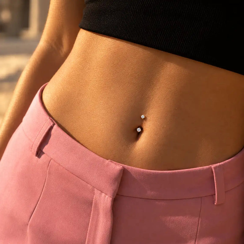 Model wearing a 14k gold prong-set curved barbell with 4mm clear gems in a belly button piercing - shown for size and placement; the amethyst version is the same size