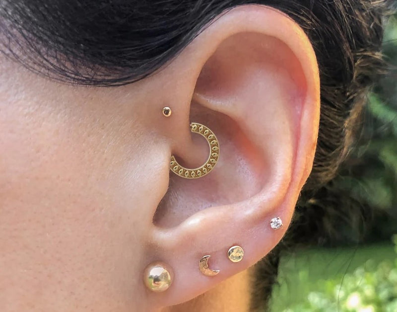 14K gold hammered moon flat back stud worn in a lobe piercing, styled with multiple gold ear piercings