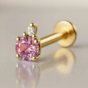 14k yellow gold flat back labret with pink tourmaline and diamond accent, angled side view on reflective surface