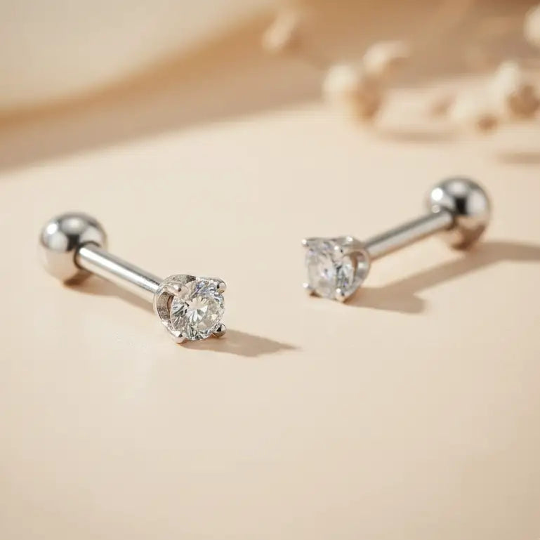 Pair of white gold cartilage studs with diamonds on a beige background