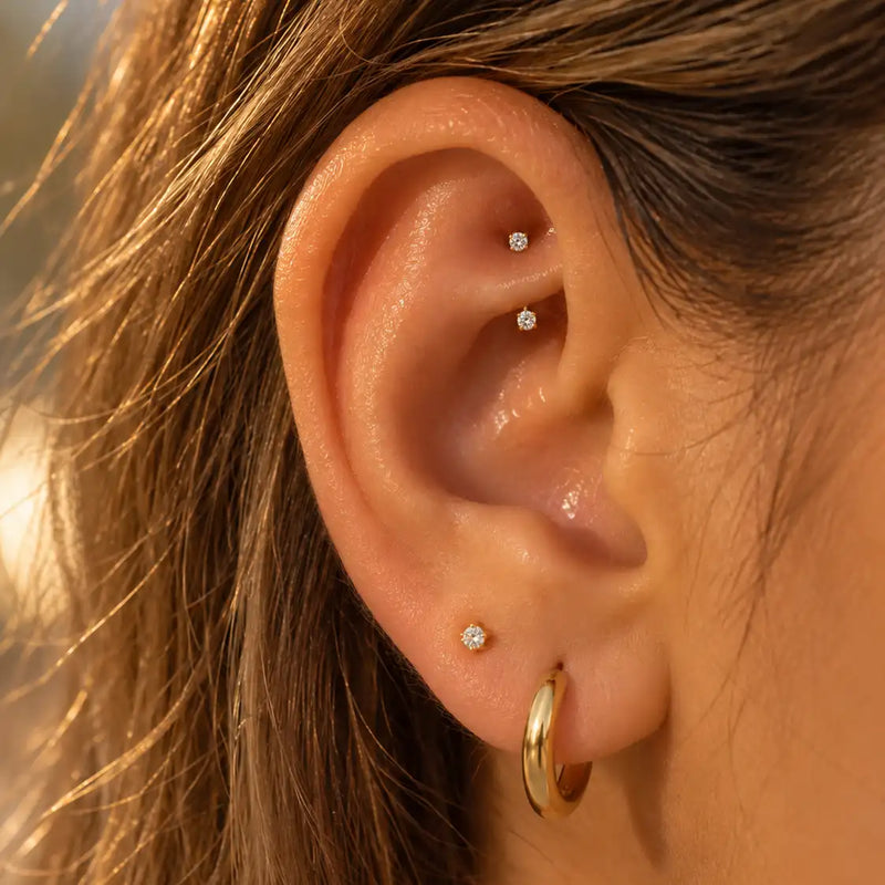 Rook piercing with a 2mm prong-set curved barbell, plus a stud and a thick gold hoop in the lobe, on a model's ear - diamond or cubic zirconia