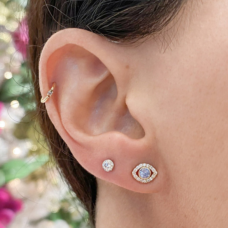 Gold CZ bezel flat back stud styled in lobe piercing alongside other gold ear jewelry