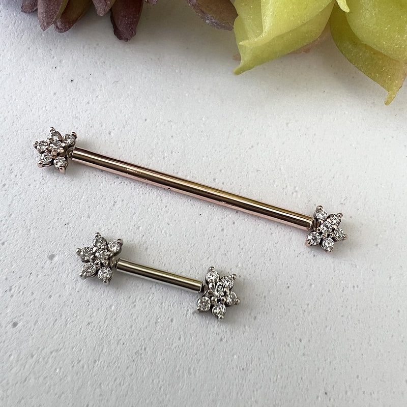 14k rose gold and white gold CZ flower nipple barbells side by side on stone surface for size comparison