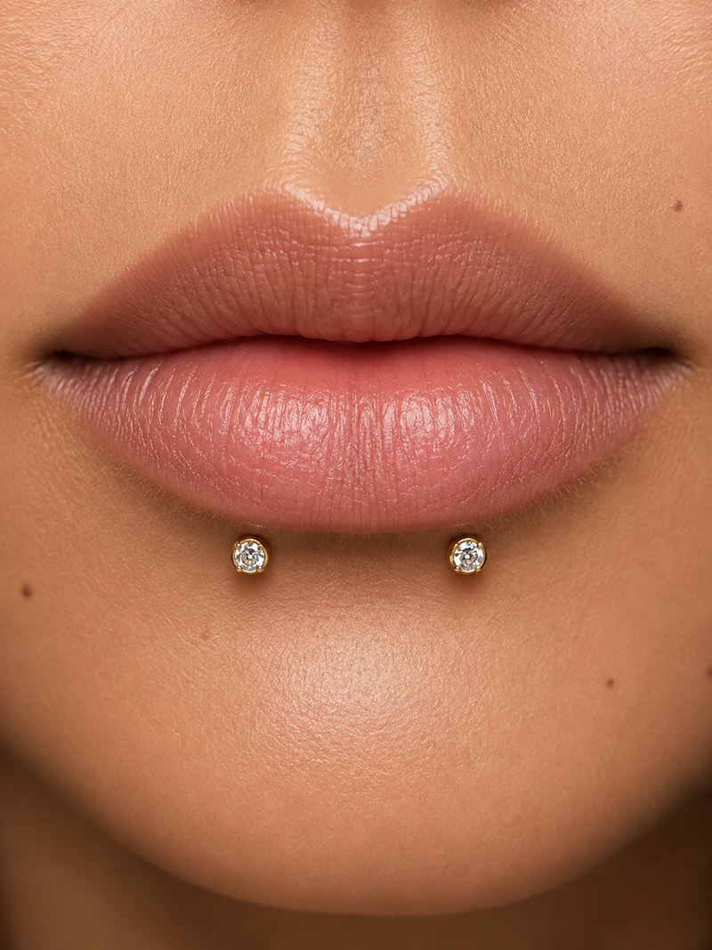 Dolphin bites piercing with two gold prong-set studs side by side, centred below the lower lip