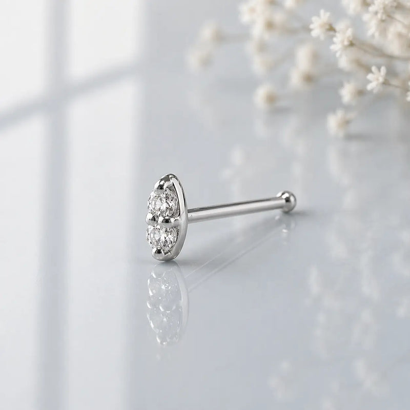 14K white gold double diamond nose bone style, angled view showing ball-end post on gray surface