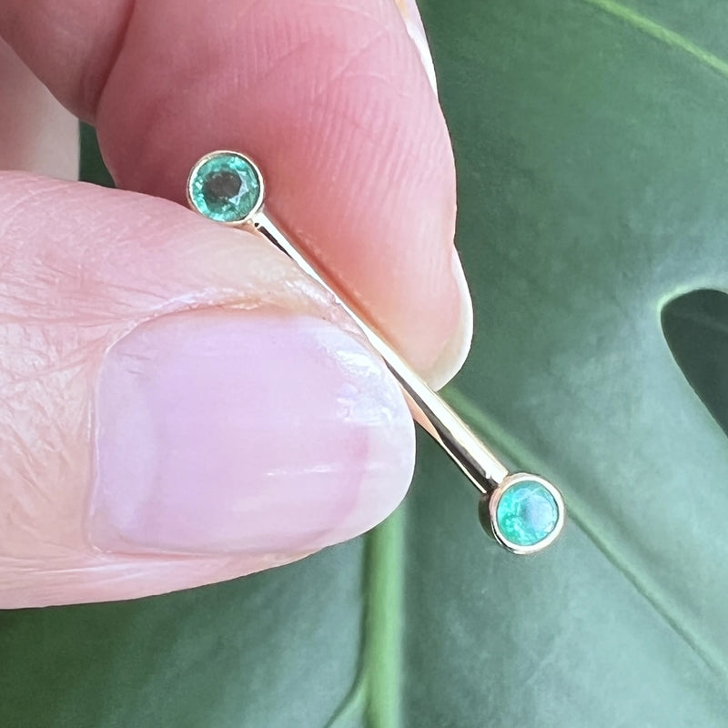 14K gold emerald bezel nipple barbell held between fingers showing size and scale