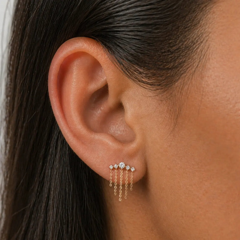 Close-up of an ear wearing a diamond and chains dangling earring with a blurred background