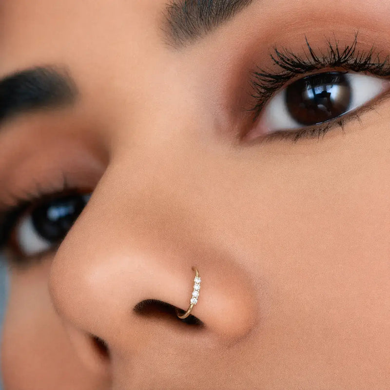 Close-up of 14K gold four-diamond nose ring hoop worn in nostril piercing with eye detail