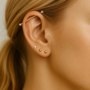 14k gold bezel-set industrial barbell worn in model's cartilage piercing, styled with gold ear studs