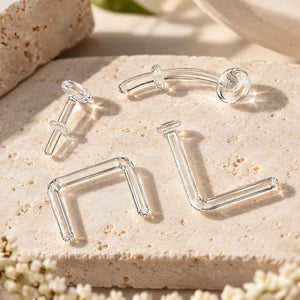 Four clear glass piercing retainers on travertine - flat back labret, curved barbell, septum staple and nose L-bend styles