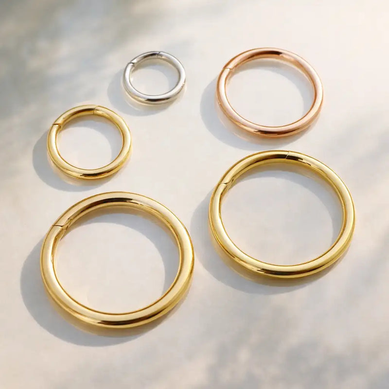 18K yellow, white, and rose gold plain clicker hoops in multiple sizes arranged on light surface