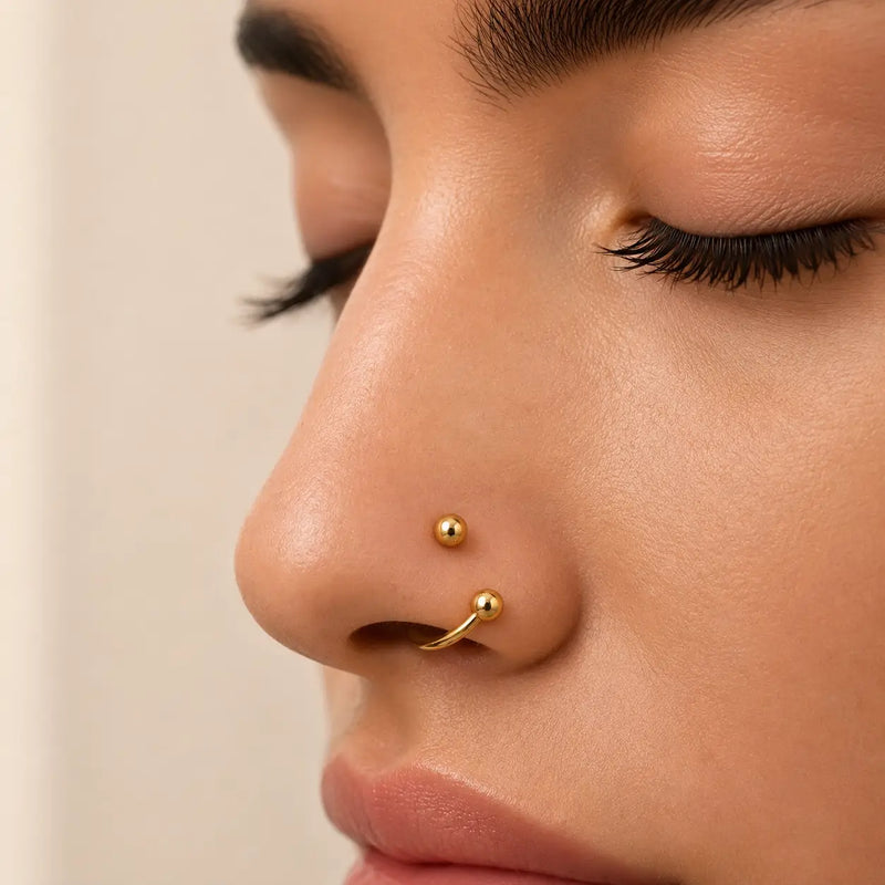 Close-up of a person's nose wearing a spiral barbell, against a soft beige background.