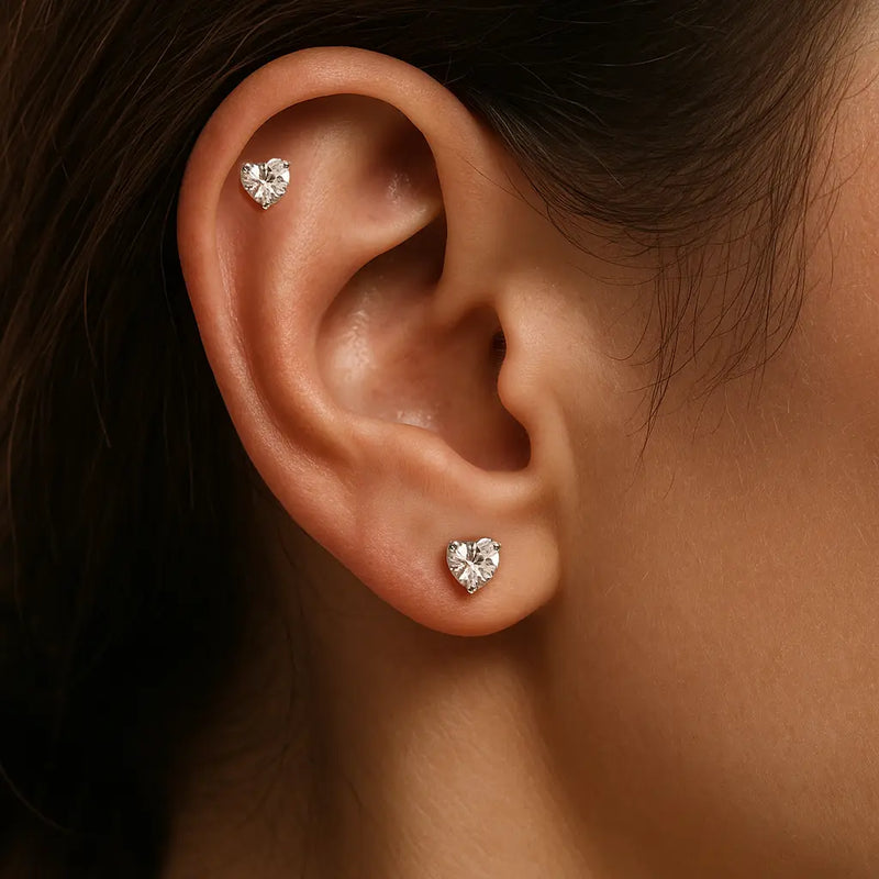 Clear CZ heart-cut 14k gold cartilage studs worn in helix and lobe piercings on a model